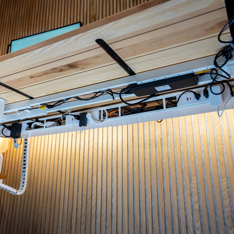 White Desky Integrated Cable & Power Channel with power outlets, neatly organizing cables under a light wood desk.