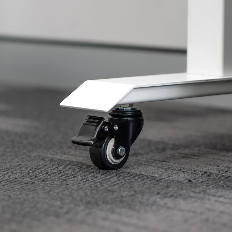 Black polyurethane locking caster wheel attached to a white steel desk leg on a gray carpet.