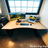 Light bamboo Desky Dual Ergo Edge sit-stand desk with a curved front, black frame, monitor, and laptop.