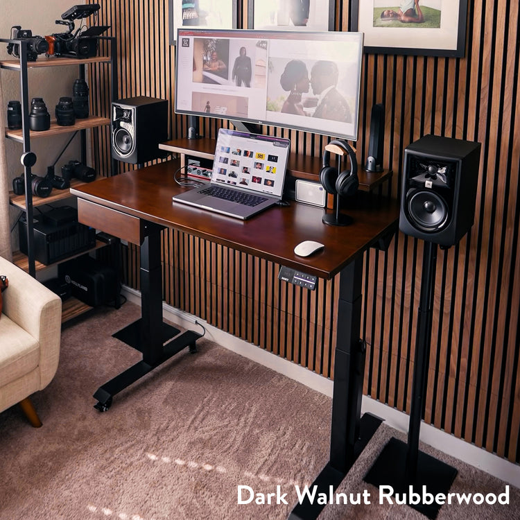 Desky Dual Rubberwood Sit Stand Desk in dark walnut with black adjustable frame, monitor, laptop, and speakers.