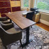 Dark brown laminate L-shaped sit-stand desk with black base, two gray chairs, and a printer.