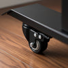 Close-up of a black steel Desky lockable desk caster with a 2" polyurethane wheel on a wooden floor.