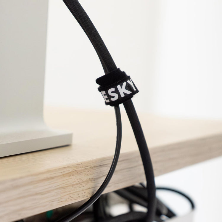 Black Desky cable organizer kit with white logo, securing a black cable to a light wood desk.