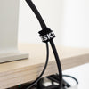 Black Desky cable organizer kit with white logo, securing a black cable to a light wood desk.