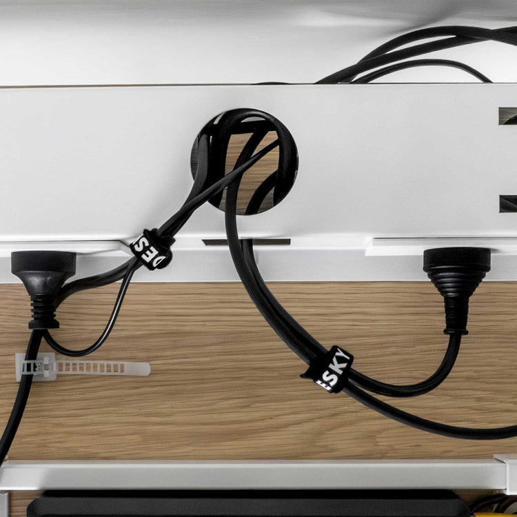 Black Desky braided polyester cable organizer sleeves tidying multiple cables under a white desk.