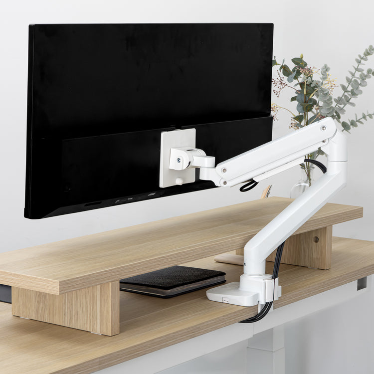 White Desky Heavy Duty Ultrawide Monitor Arm securely holding a large black monitor on a light wood desk.