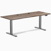 Desky Dual Laminate Sit Stand Desk with Natural Walnut top, Space Gray frame, and two grommets.