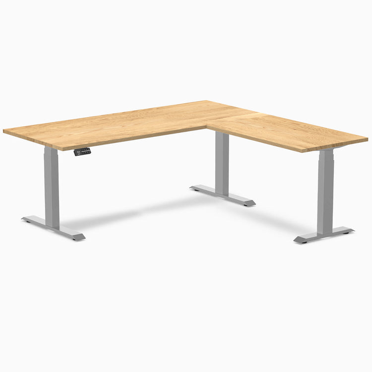 White oak L-shape sit-stand desk with gray frame and control panel.