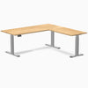 White oak L-shape sit-stand desk with gray frame and control panel.